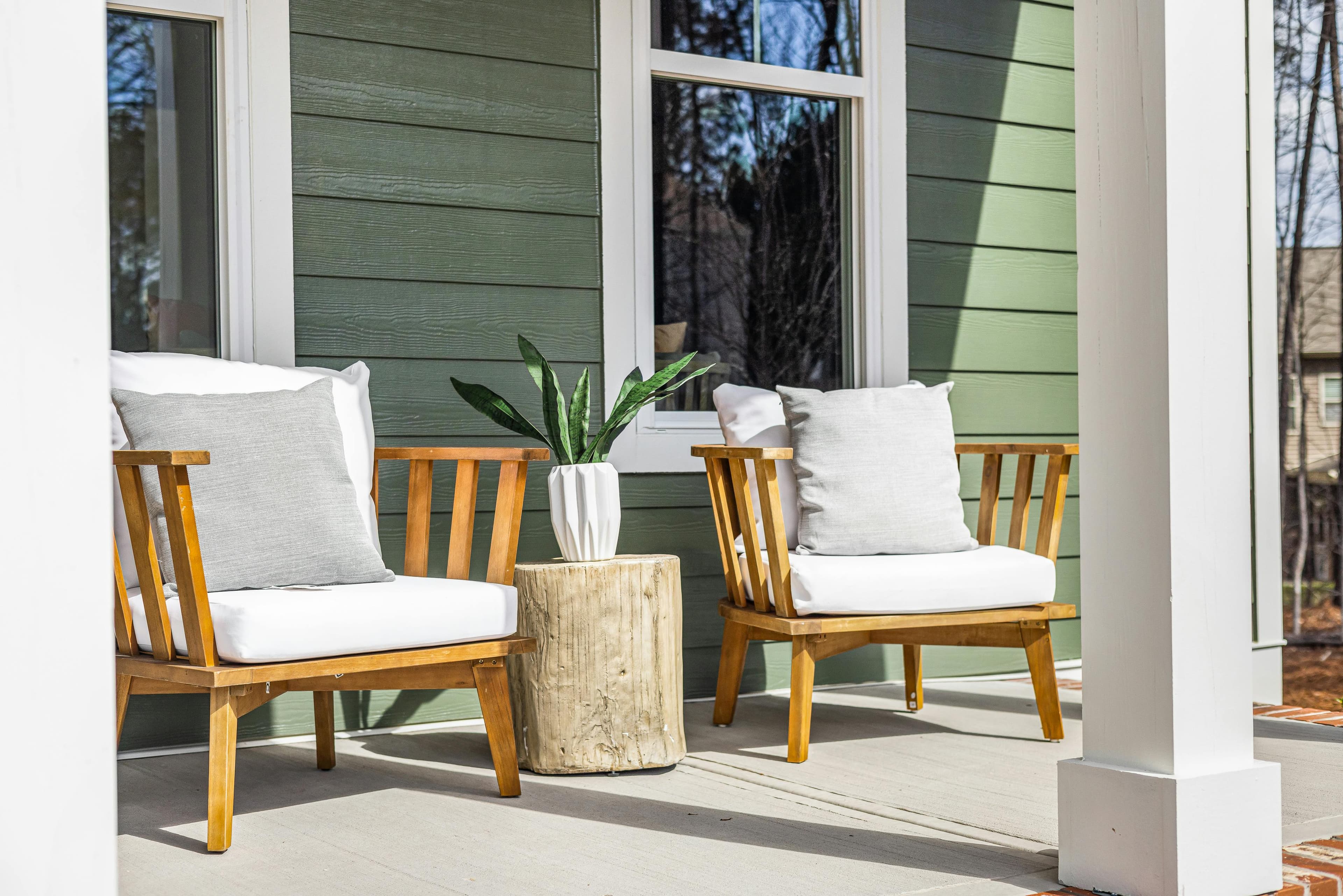 A sage-green home's front porch with wood chairs and a potted plant